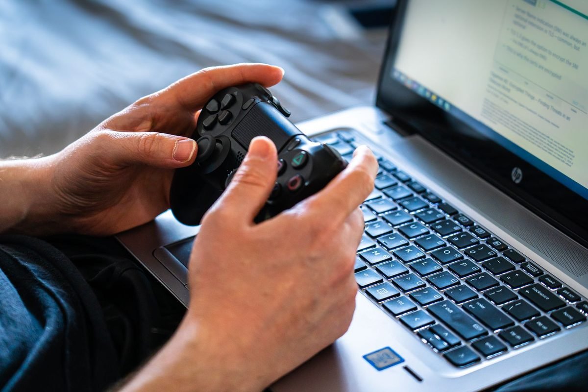 Hands holding a game controller on top of a laptop keyboard