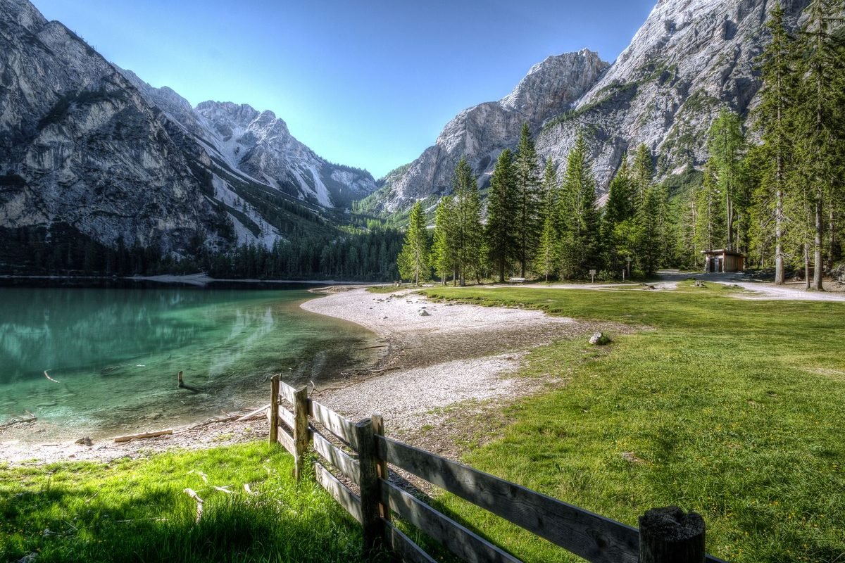 Mountain lake landscape with a green meadow and a wooden fence