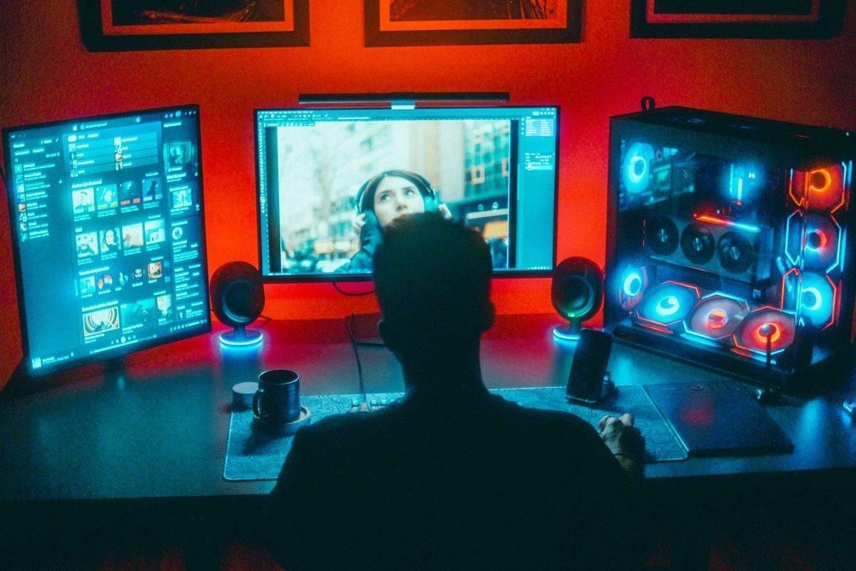 Gamer at a desk with several monitors and red and blue lighting in a dark room
