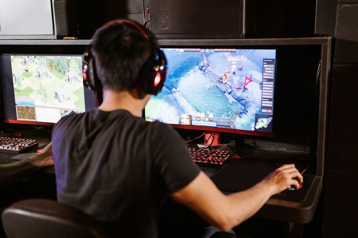 Gamer wearing headphones playing a strategy game on two monitors