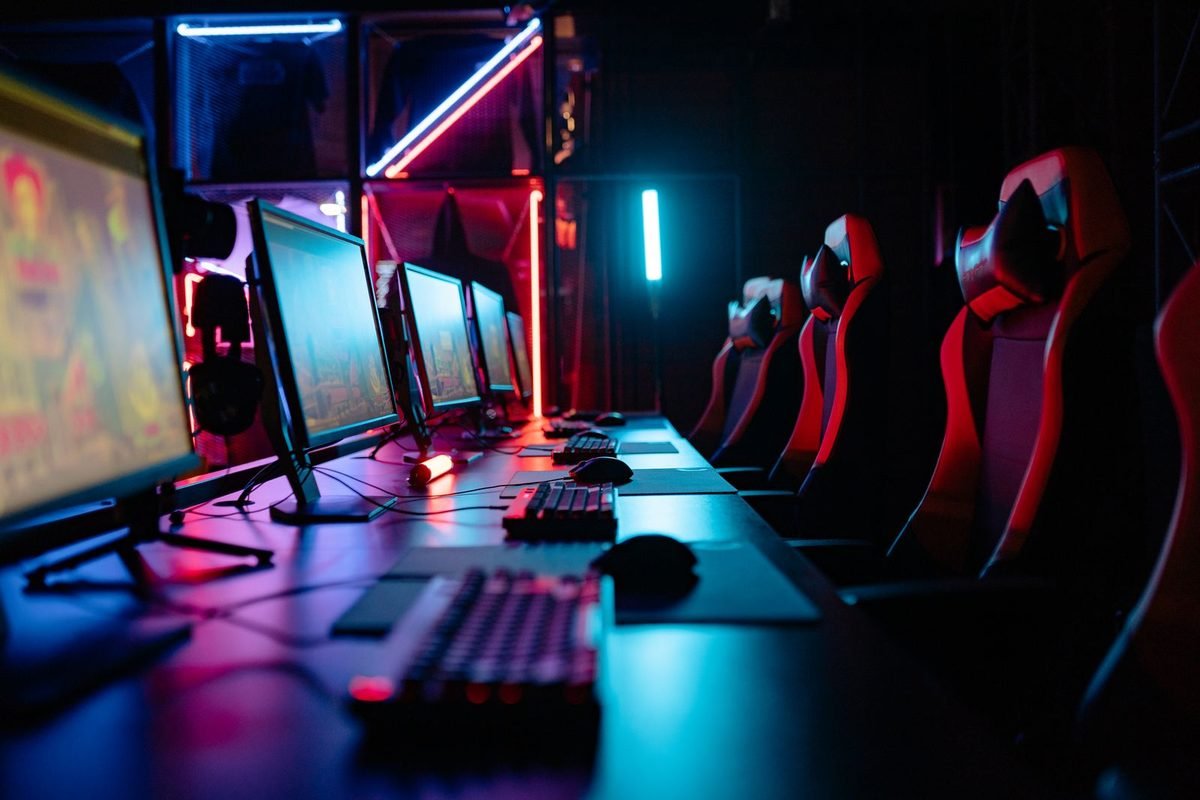 Esports room with rows of gaming monitors, keyboards and red chairs under neon lights