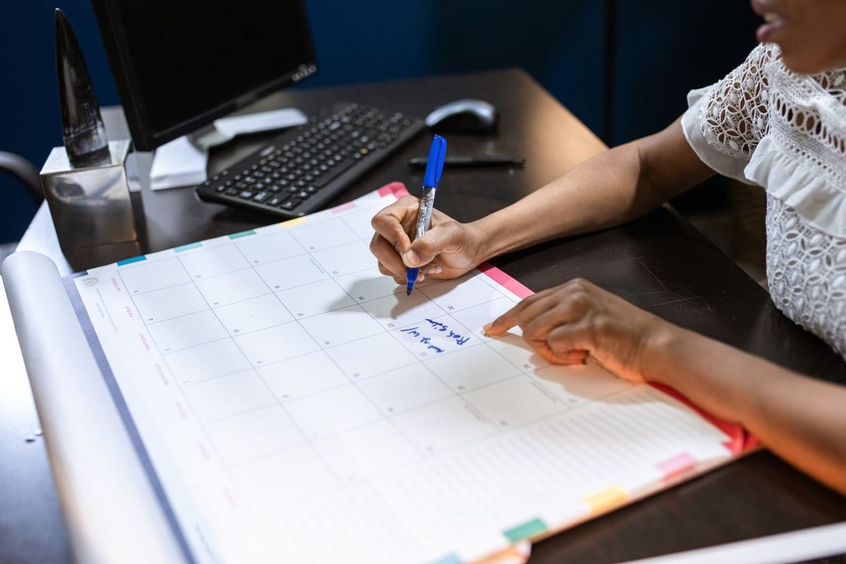 Person writing in a large monthly planner at a desk