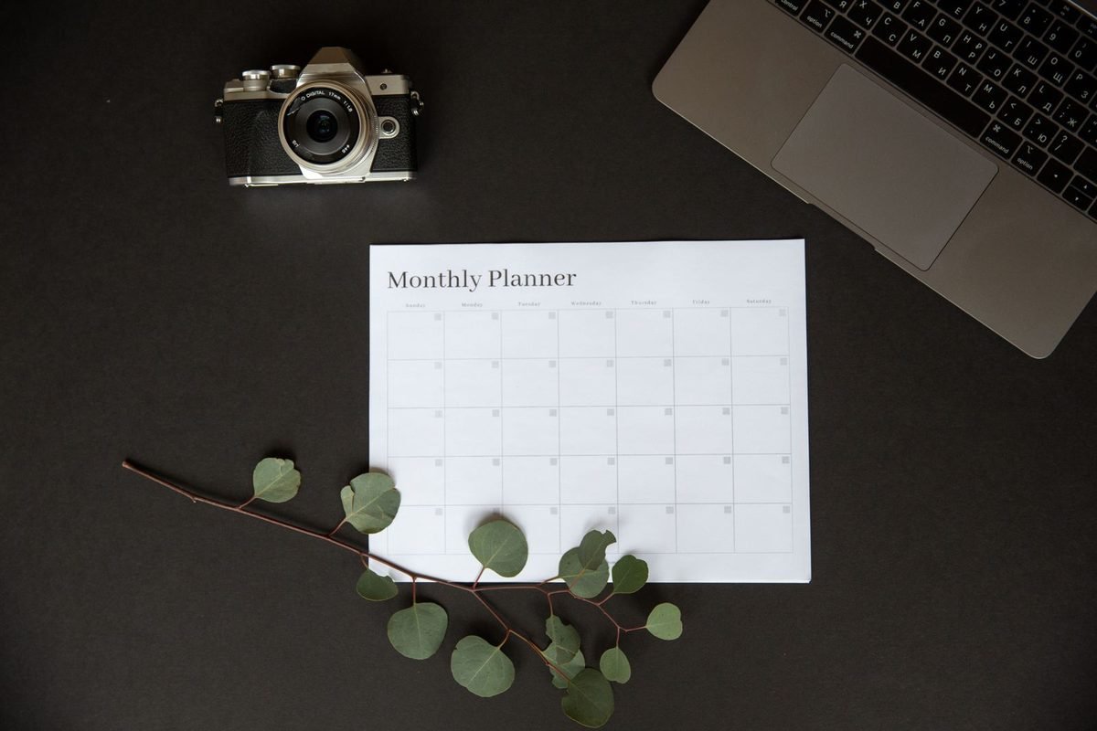 Monthly planner on a dark desk next to a camera and laptop