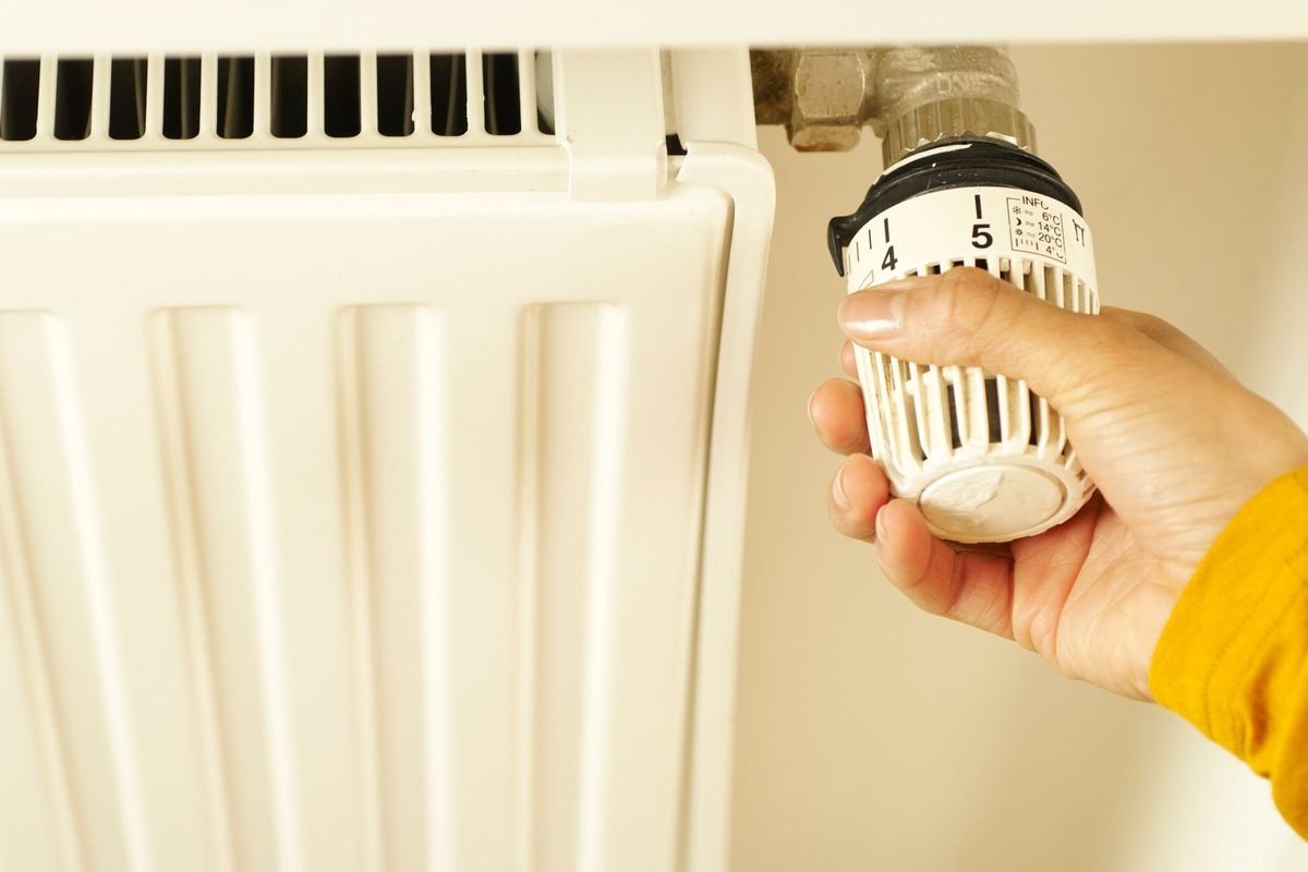 Hand turning the thermostat valve of a white radiator