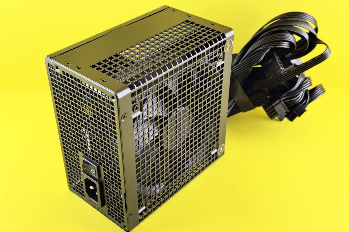 Black computer power supply unit with cables and a metal grille on a yellow background