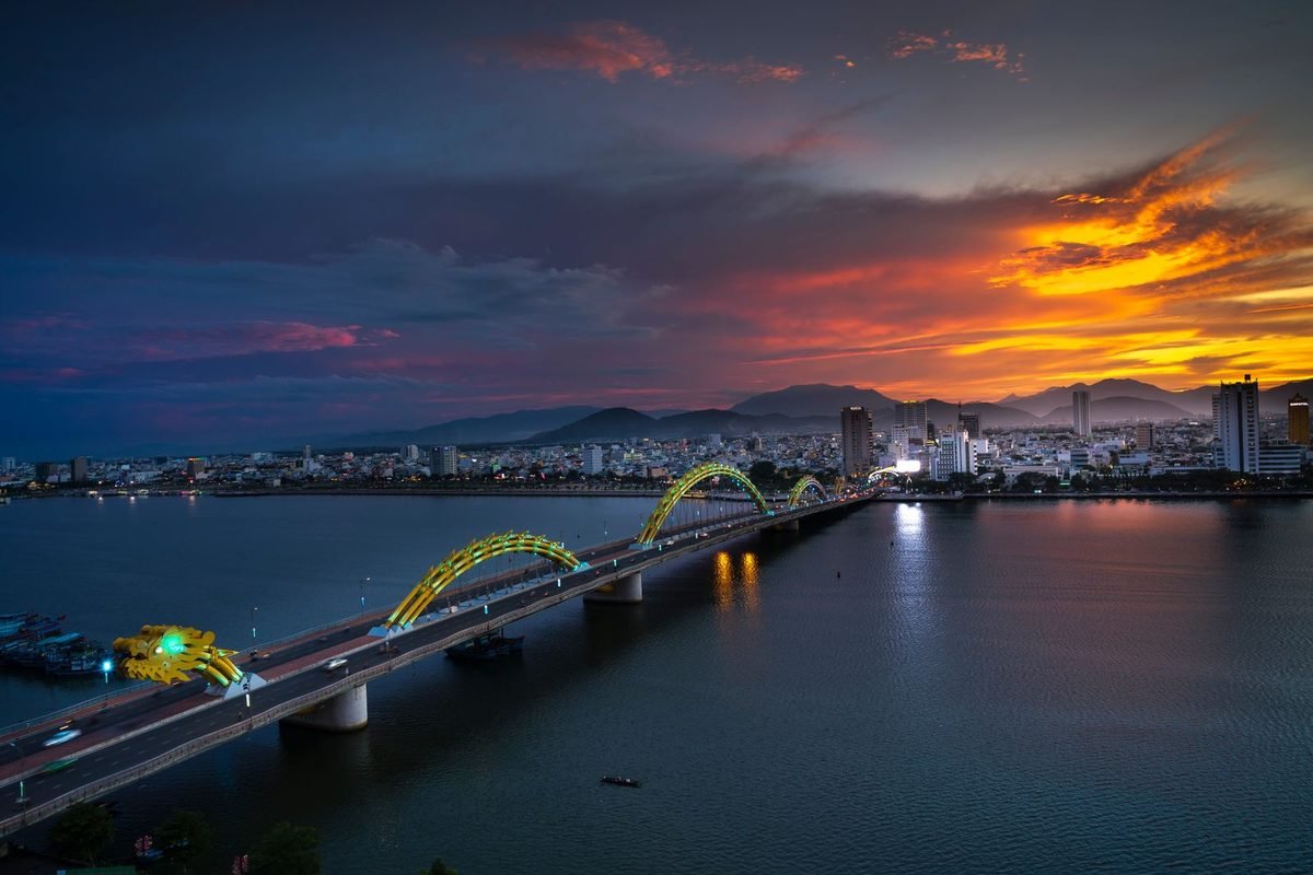 Illuminated bridge and city skyline under a vivid orange sunset sky